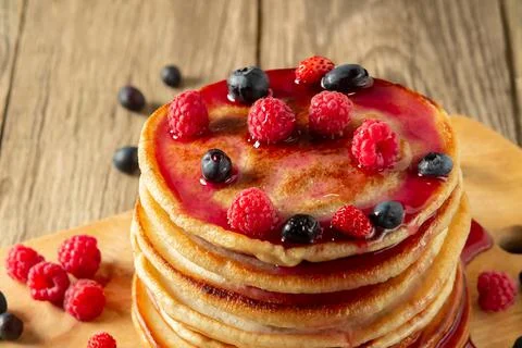 Stack of pancakes with syrup and fresh berries on wooden board on table Stock Photos