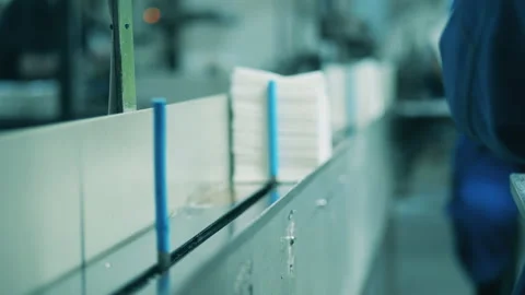 Stack of paper napkins being placed onto a conveyor by a factory worker Stock Footage 148331036