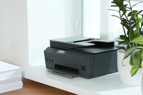 Stack of paper on wooden table near window sill with modern printer in office Stock Photos