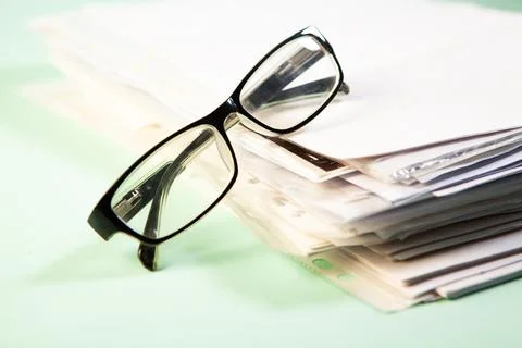 Stack of papers and eyeglasses on green background. Selective focus. Stock Photos