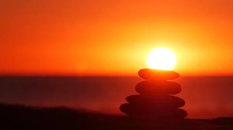 Stack of pebble stones, sandy ocean beach, sunset sky. Rock balancing by water. Foto stock