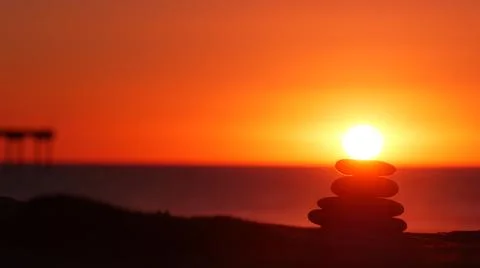 Stack of pebble stones, sandy ocean beach, sunset sky. Rock balancing by water. Foto stock