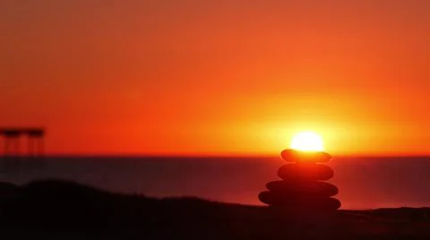 Stack of pebble stones, sandy ocean beach, sunset sky. Rock balancing by water. Foto stock