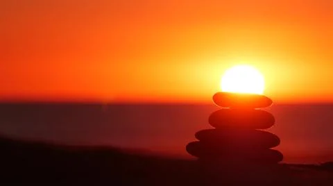 Stack of pebble stones, sandy ocean beach, sunset sky. Rock balancing by water. Foto stock