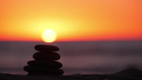 Stack of pebble stones, sandy ocean beach, sunset sky. Rock balancing by water. Foto stock