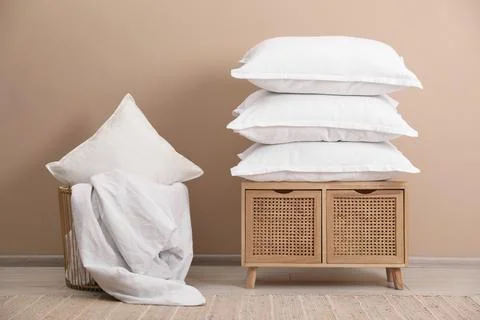 Stack of pillows, storage cabinet, basket and blanket near beige wall Stockfoto's