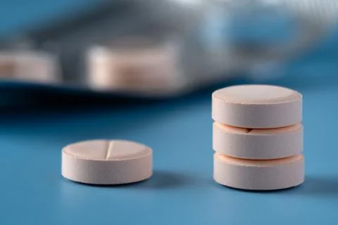 A stack of pills with one on the side on a blue surface Stock Photos