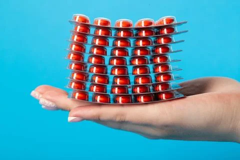 Stack of pills on the palm of the hand on a blue background, close-up. Concept 스톡 사진