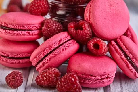 A stack of pink macarons surrounded by raspberries on a wooden table Stock Photos