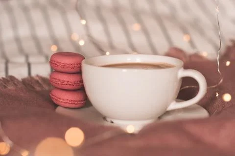 Stack of pink macaroons with cup of coffee in bed over lights at background c Stock Photos