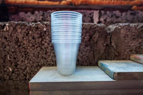 Stack of Plastic Cups on Dusty Workshop Shelf by Volcanic Stone Wall 库存照片
