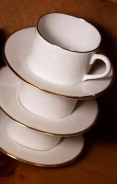 Stack of porcelain coffee cups with gold rim on wooden background Stock Photos