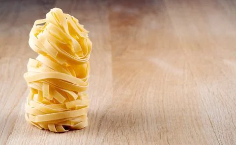 Stack of raw tagliatelle pasta nests on a wooden table with copy space Fotos de archivo