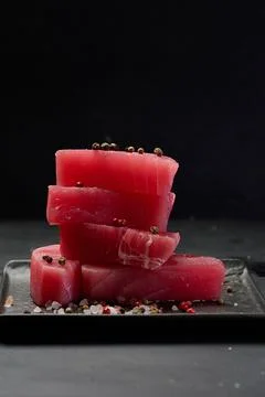Stack of raw tuna pieces on black square plate, black background Stock Photos