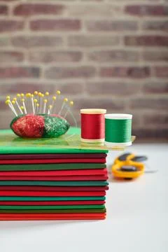Stack of red and green fabrics, sewing and quilting accessories on brick wa.. 스톡 사진