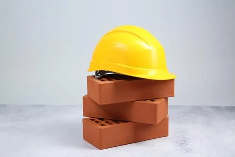 Stack of red bricks and hard hat on textured table against light background.. Stockfoto's
