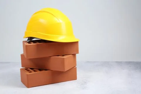 Stack of red bricks and hard hat on textured table against light background.. Stock Photos