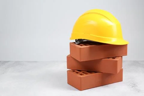 Stack of red bricks and hard hat on textured table against light background.. Stock Photos