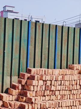 A stack of red bricks on the background of a green wooden fence. 写真素材