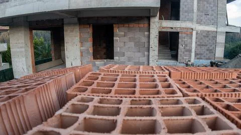 Stack of red clay bricks in the foreground of a building construction site Stock Photos