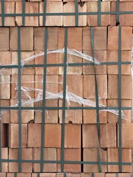 Stack of red clay bricks with plastic wrap and green straps, ideal for cons.. 写真素材
