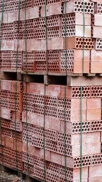A stack of red hollow clay bricks secured with green straps on wooden pallets Stock Photos