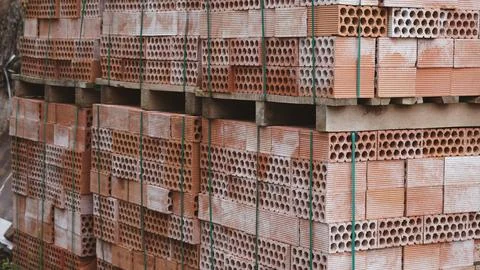 A stack of red hollow clay bricks secured with green straps on wooden pallets Stock Photos
