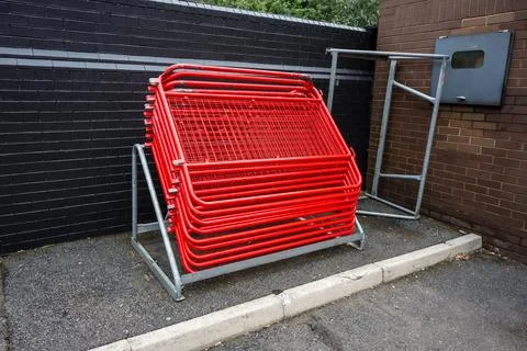 Stack of red metal barriers neatly arranged on a rack against a black brick.. Stock Photos