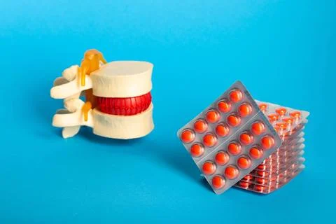 Stack of red pills on the background of the lumbar spine and blue background Stock Photos