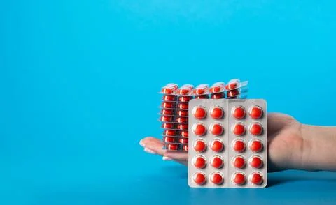 Stack of red pills in hand on blue background for edema. Diuretic pills for Stockfoto's