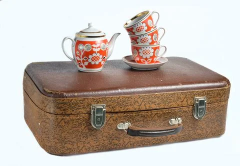 A stack of retro cups and a ceramic teapot on old leather suitcase isolated o Stock Photos