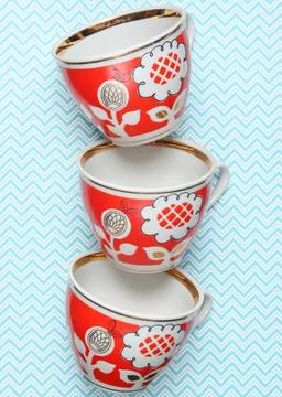 Stack of retro cups with red patterns on a tablecloth. Stock Photos
