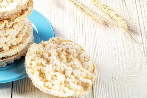 A stack of rice biscuits on a blue saucer and ears of barley on a wooden tabl Stock Photos