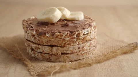A stack of rice cakes with chocolate spread and banana slices on burlap clo.. Video stock 332910658