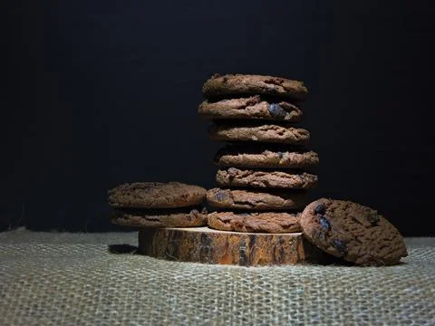 A stack of rich chocolate cookies with visible chocolate chips sits on a ru.. 스톡 사진