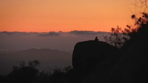 Stack of rocks atop boulder, sea of clouds in background.  City below with Stock Footage 100575320