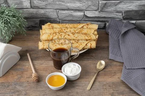 Stack of rolled pancakes with honey, yogurt, and coffee on a table with sto.. Stock Photos