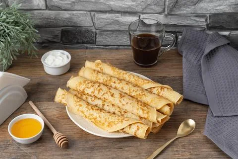 Stack of rolled pancakes with honey, yogurt, and coffee on a table Stock Photos