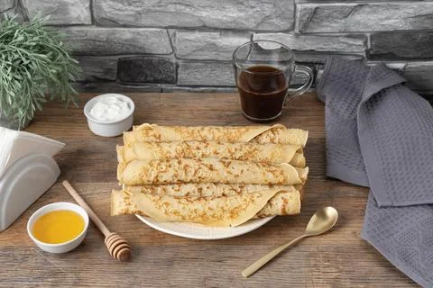 Stack of rolled pancakes with honey, yogurt, and coffee on a table with sto.. Stock Photos