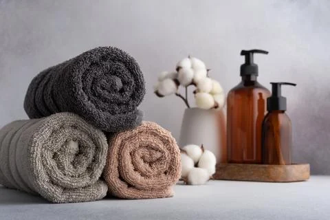 Stack of rolled towels with cotton flowers and dispenser bottles on gray back Stock Photos