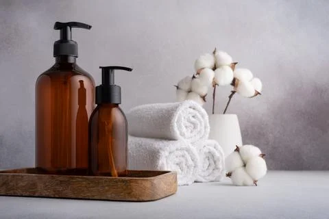 Stack of rolled white towels with cotton flowers and dispenser bottles on gra Stock Photos