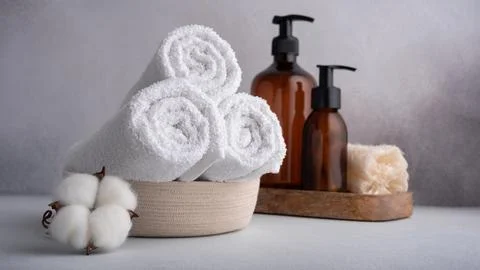 Stack of rolled white towels with cotton flowers and dispenser bottles on gra 库存照片