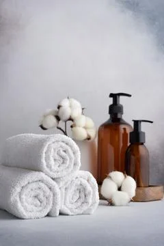 Stack of rolled white towels with cotton flowers and dispenser bottles on gra Stock Photos