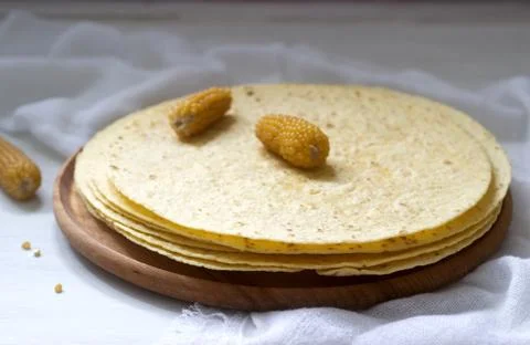 A stack of round corn tortillas on a wooden board and corncobs. Stock-Fotos