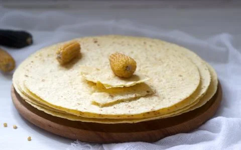 A stack of round corn tortillas on a wooden board and corncobs. Stock-Fotos