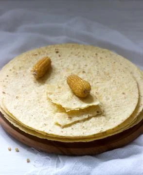 A stack of round corn tortillas on a wooden board and corncobs. Stockfoto's