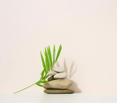 Stack of round stones and and green palm leaf on a beige background. Scene fo Fotos Stock