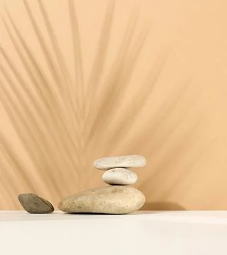 Stack of round stones and and the shadow of a palm leaf on a beige background Stockfoto's