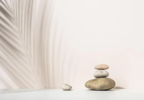 Stack of round stones and and the shadow of a palm leaf on a beige background Foto stock
