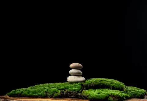 Stack of round stones on green moss, black background. Podium to showcase pro Stock-Fotos